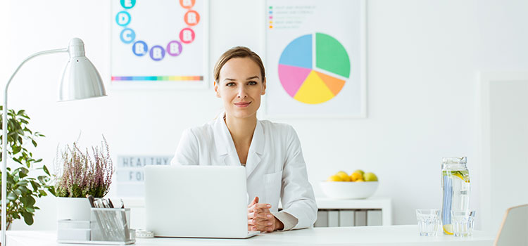 young female dietitian sitting at desk with food charts in the background