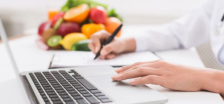 woman taking notes next to laptop and fruit