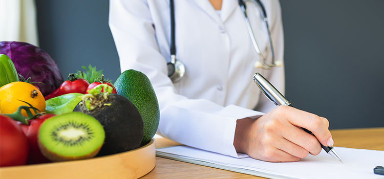 female dietitian with stethoscope writing on pad next to a bowl of fruit