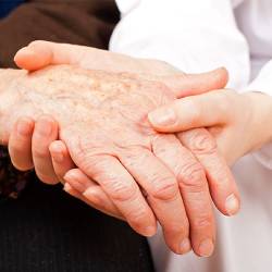 massage therapist holding hand of elderly patient during palliative massage