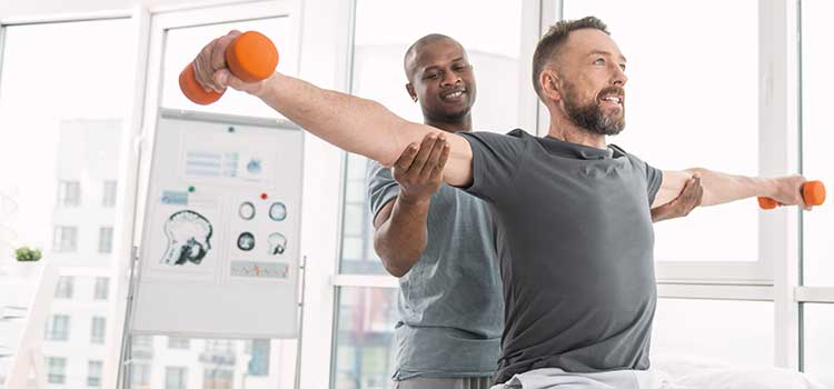male physical therapist helps rehab patient straighten arms with weights